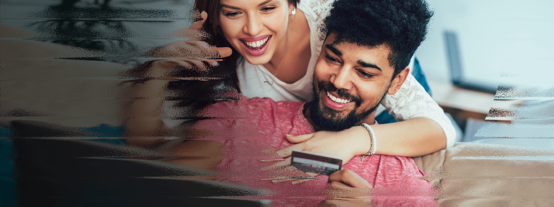 A couple smiles at their laptop screen while holding a credit card