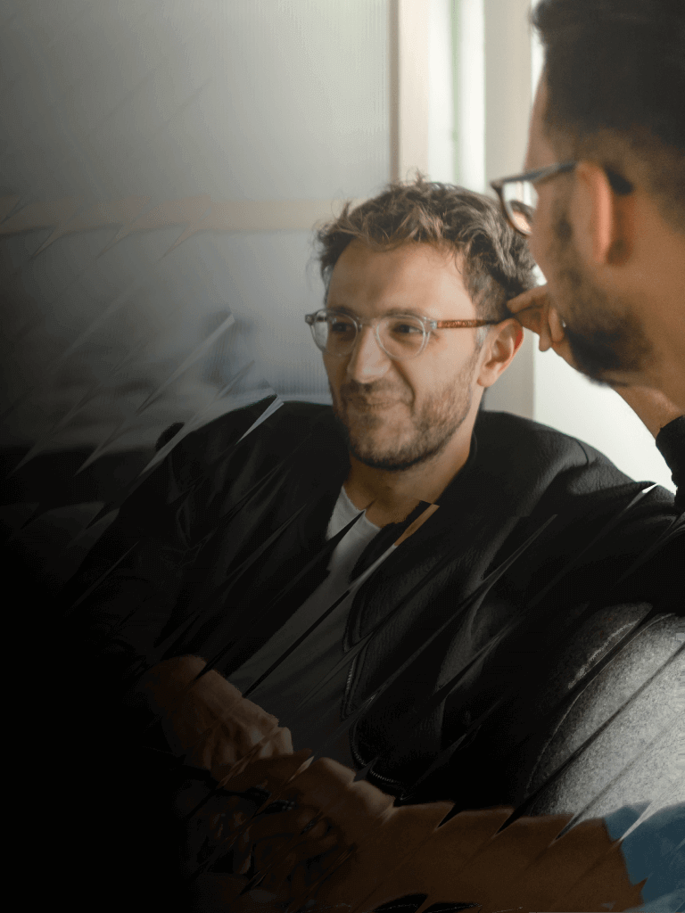 Three people sit in a casual meeting space, smiling while discussing something