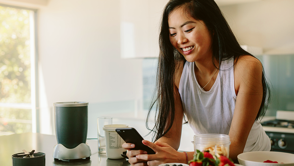 Image of a woman holding her phone and making a smoothie