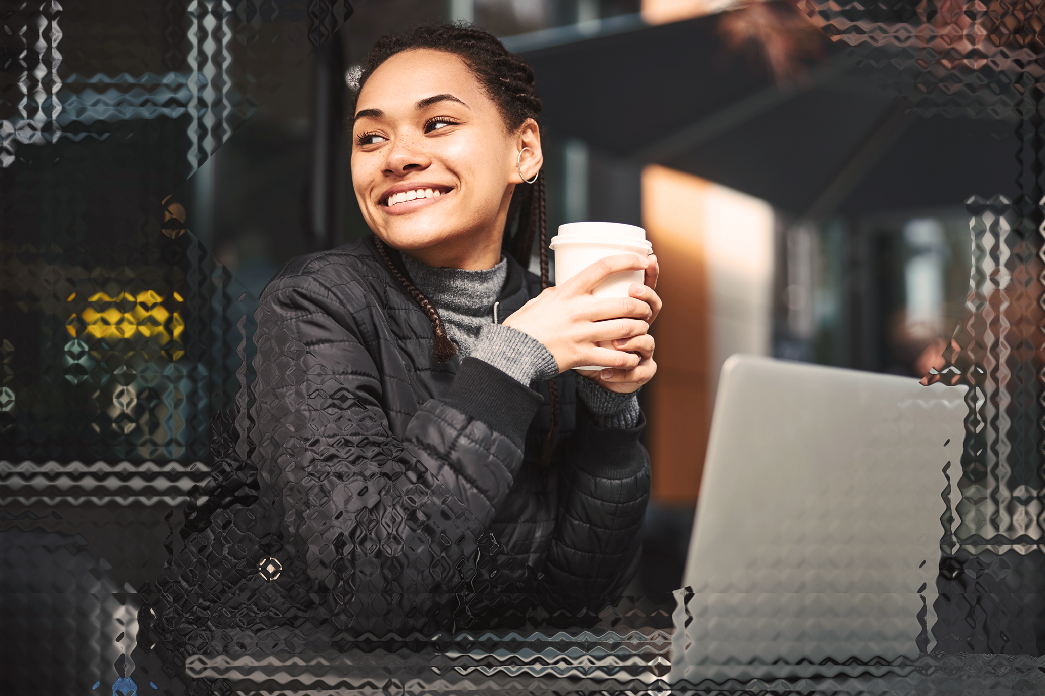 Smiling woman holding a cup of coffee in front of a laptop.
